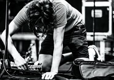 Black and white image of a person plugging in a pedalboard on stage