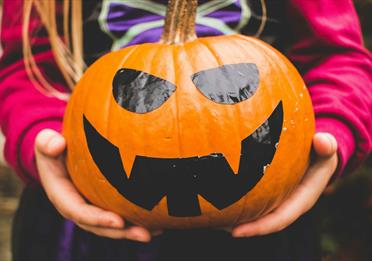 Girl in witch costume holding a smiling pumpkin