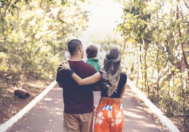 Young family walking in a light forest and carrying their toddler