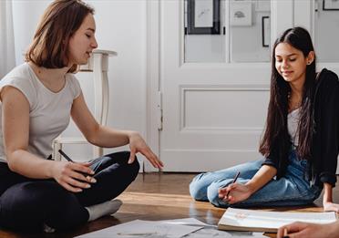 Two people sat on the floor between art supplies