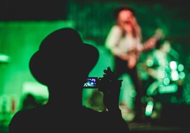 Person recording video of a person playing guitar onstage