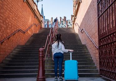 Girl at the bottom of a set of steps holding a suitcase