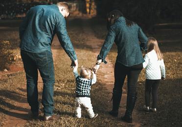 Young family walking a green forest and holding hands with their toddler