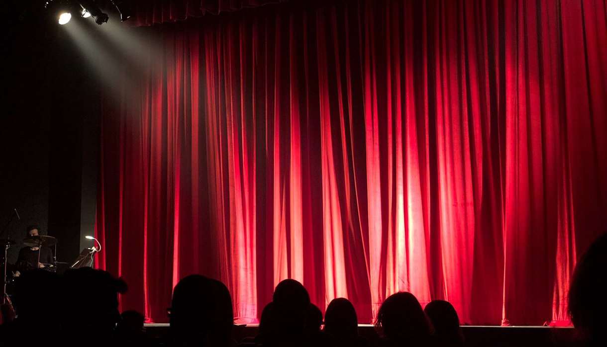 People sitting in a theatre in front of a red curtain