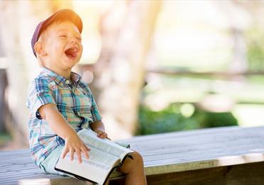 Boy sitting with book on a bench and laughing