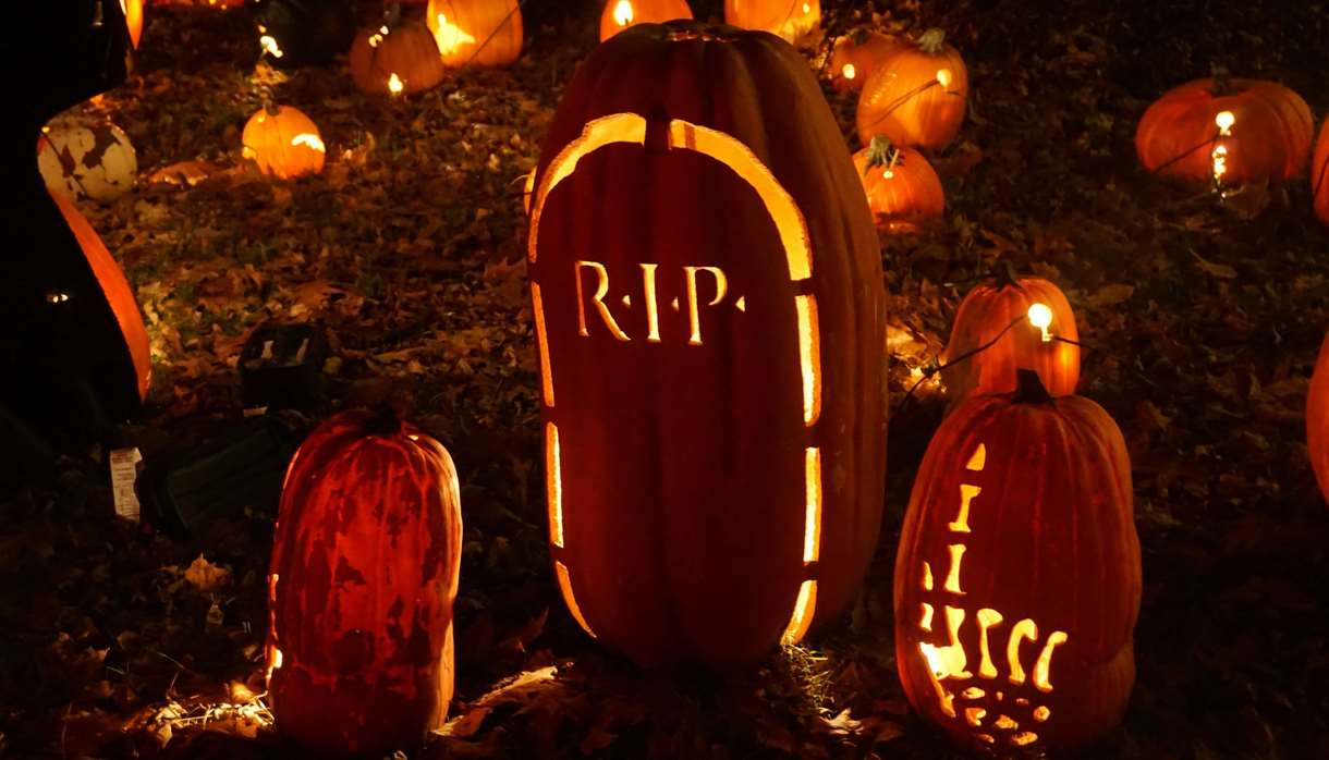 Two pumpkins carved with a skeleton hand pointing up and a tombstone