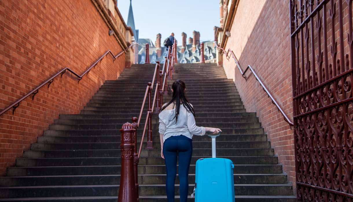 Girl at the bottom of a set of steps holding a suitcase