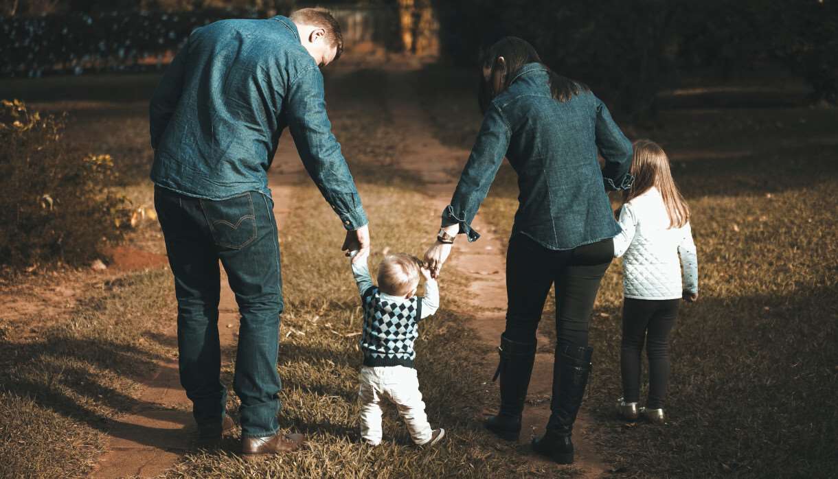 Young family walking a green forest and holding hands with their toddler