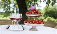 Et bord med glass med rose og et steltfat med jordbær i hagen til Klækken hotell.