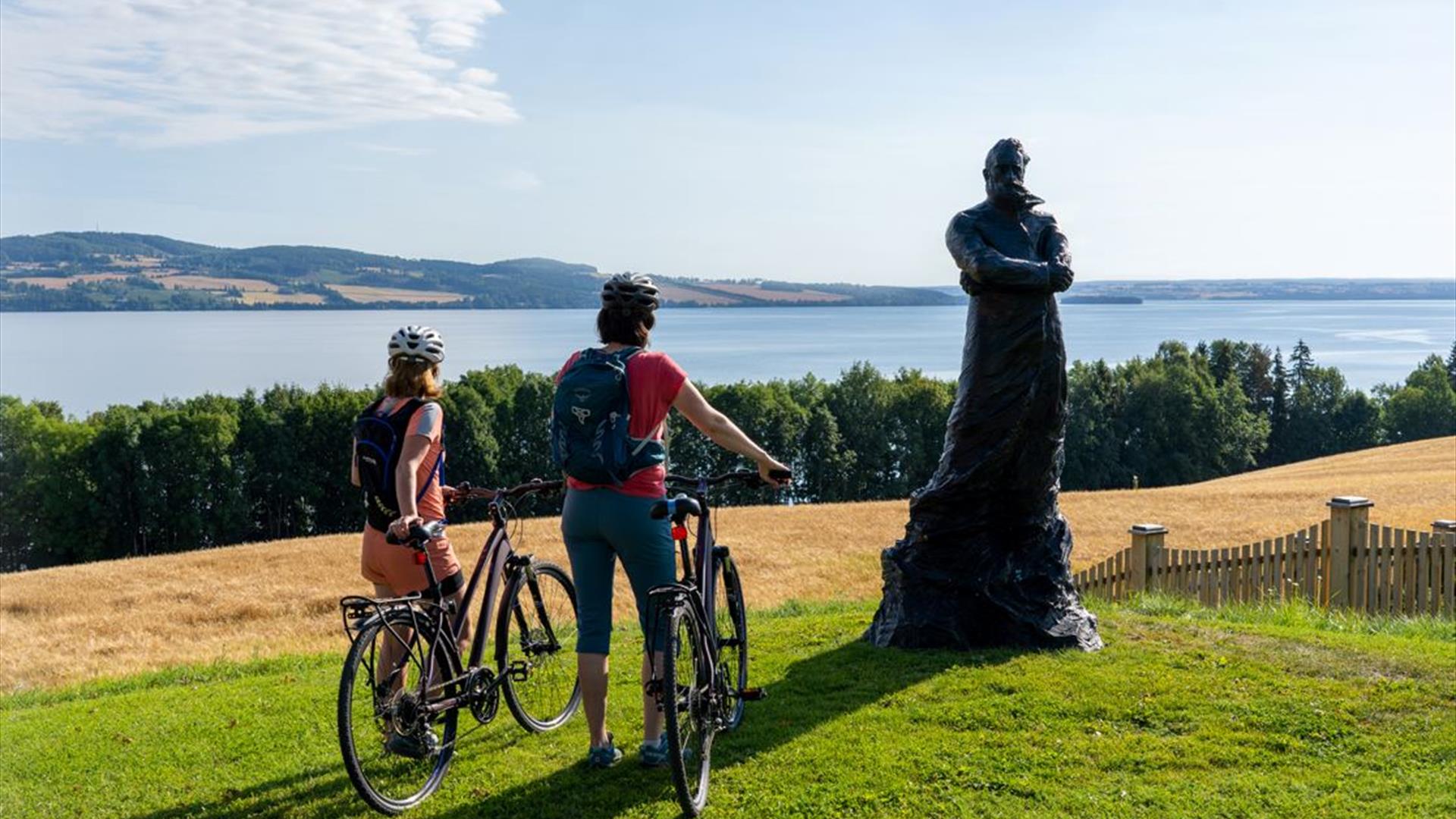 Peder Balke-senteret på Kapp i Østre Toten. Mjøstråkk-syklister nyter Mjøsutsikten ved Peder Balke statue.