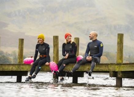 Group sitting on a pier in wetsuits after a wild swim in the Lake District
