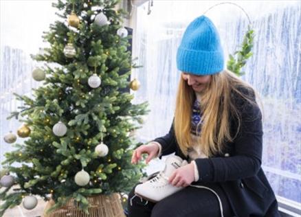 Woman laces a figure skating boot in front of a decorated Christmas tree