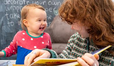 A kid laughing at an adult who is reading them a book