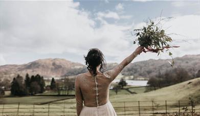 Bride with Raised Bouquet Overlooking Scenic Views from a Wedding at Allan Bank in Grasmere, Lake District