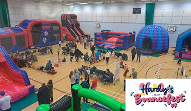 Indoor family fun event with large inflatable obstacle courses, bouncy castles, slides, and activity areas. Children and parents are playing, while ot