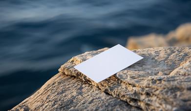 a piece of a paper sat at the end of a rock overhanging a body of water