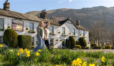 Couple walking with daffodils in front of The Swan at Grasmere in the Lake District, Cumbria