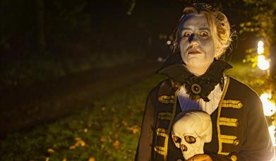 Women in white make up holding a human skull stood in a field lit by candlelight
