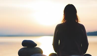 photo of a silhouetted person sat looking over the ocean