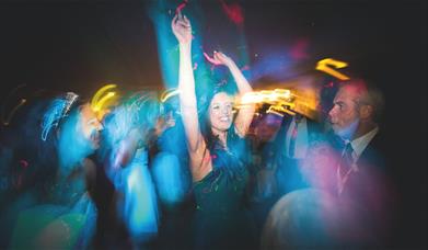 A woman in a dark dress with her arms raised, appearing to be dancing or celebrating