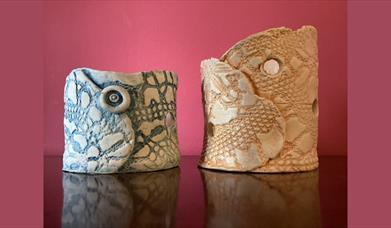 Two handmade ceramic owl sculptures with textured lace patterns, one in blue tones and the other in beige