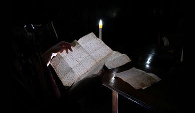a person reading a page of Mary Shelley's Frankenstein in a dark room only visible by candlelight