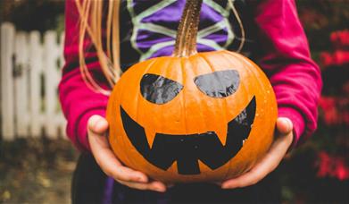 A girl holding a pumpkin with a face drawn on it