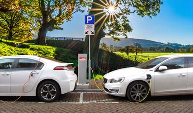 Two electric vehicles charging in a car park with a scenic backdrop