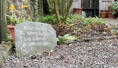 Front garden featuring a stone engraved with the words: A soft sky was among the hills and summer sunshine above.