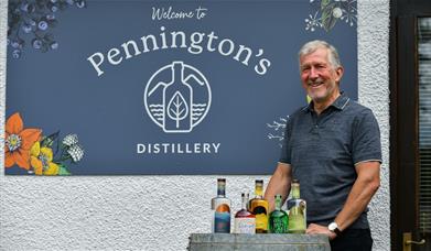 Mike Pennington posing with Pennington's Spirits in front of the sign for the distillery in Kendal, Cumbria © Christopher Holmes Photography