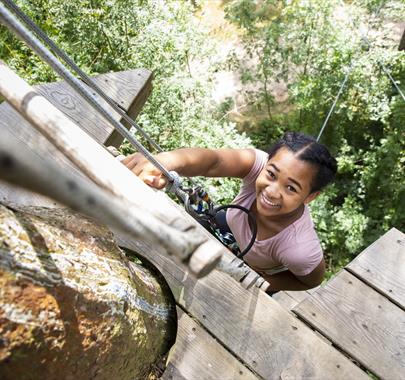 a smiling child climbing up a ladder on a high rise rope course