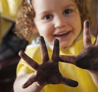 Smiling child holding up hands covered in dirt, showing them proudly