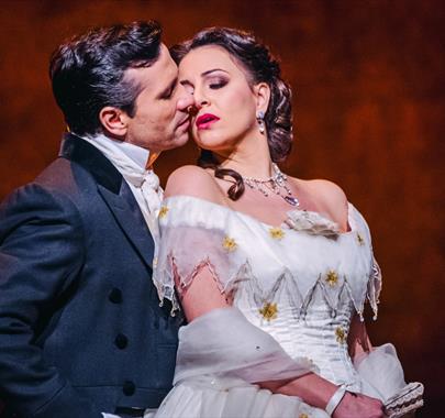 A man stood closely behind a women with the women leaning back looking in a romantic manner