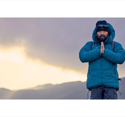 Krish Thapa poses atop a mountain with a sunrise in the background