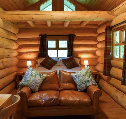 Interior of The Cabin at Grizedale Forest, with a double bed, sofa, small kitchenette, and dining table for two.