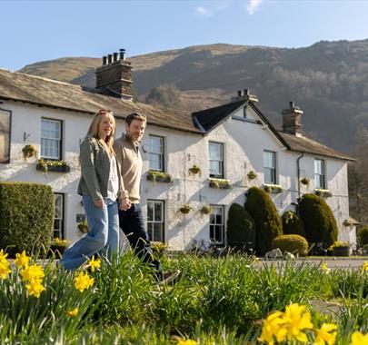 Couple walking with daffodils in front of The Swan at Grasmere in the Lake District, Cumbria
