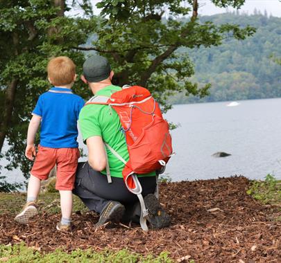 a child and an adult (wearing hiking gear and a backpack) looking over a lake