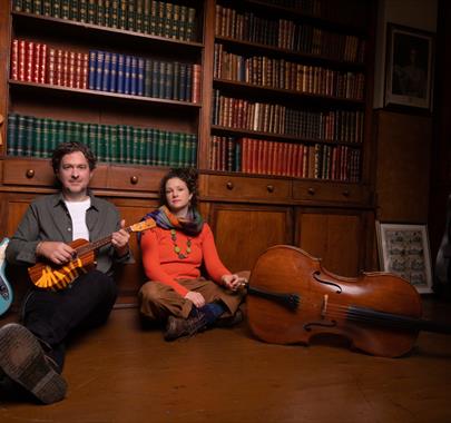 Band members sitting on the floor in a library holding ukulele