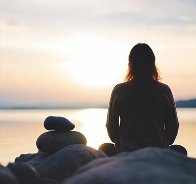 photo of a silhouetted person sat looking over the ocean