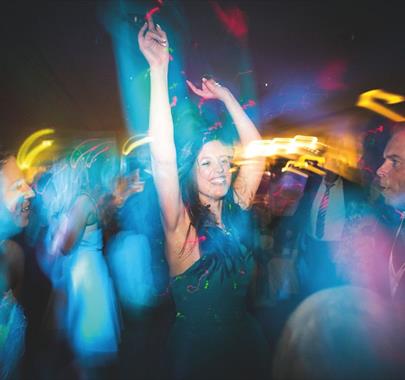 A woman in a dark dress with her arms raised, appearing to be dancing or celebrating