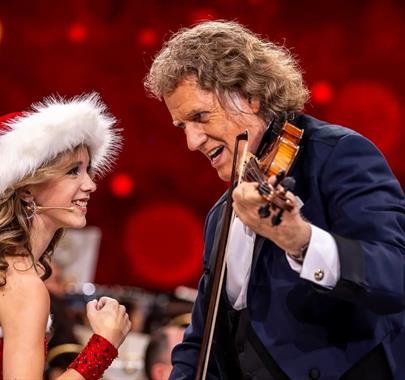 Photo of André Rieu playing the violin next to a women who is wearing a santa hat