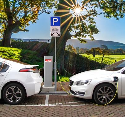 Two electric vehicles charging in a car park with a scenic backdrop