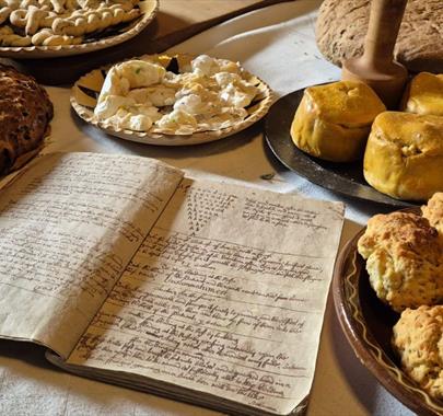 household recipe book from the 17th century accompanied by food from the same period laid out on a table.