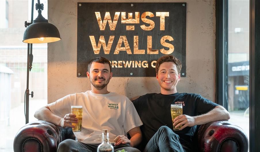 Founders of West Walls Brewing Co, seated inside the brewery, holding beers in Carlisle, Cumbria