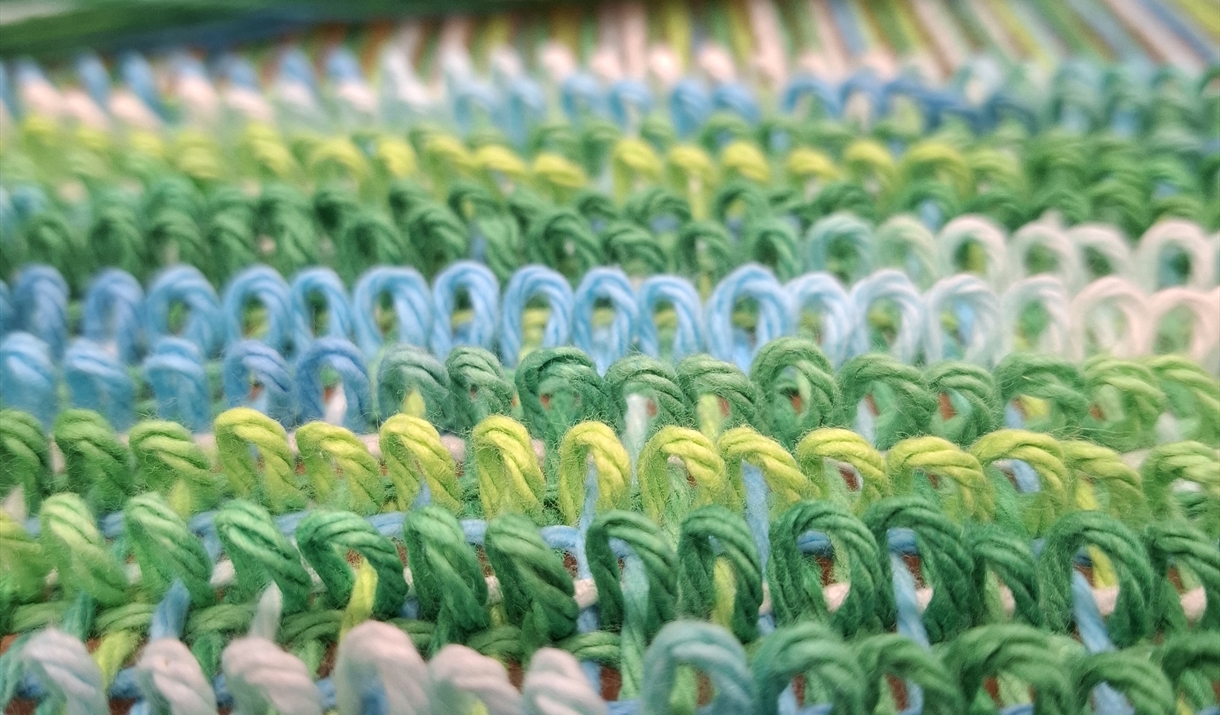 Close-up of a weaving loom featuring vibrant green and blue yarns interlaced in the weaving process.