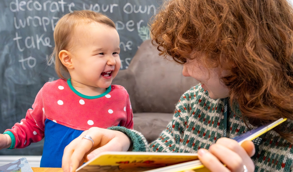 A kid laughing at an adult who is reading them a book