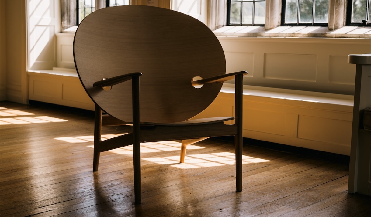 A wooden chair with a large rounded back dappled in sunlight