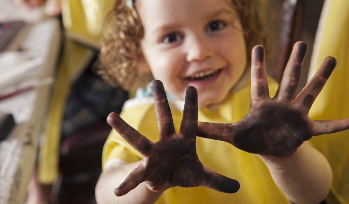 Smiling child holding up hands covered in dirt, showing them proudly