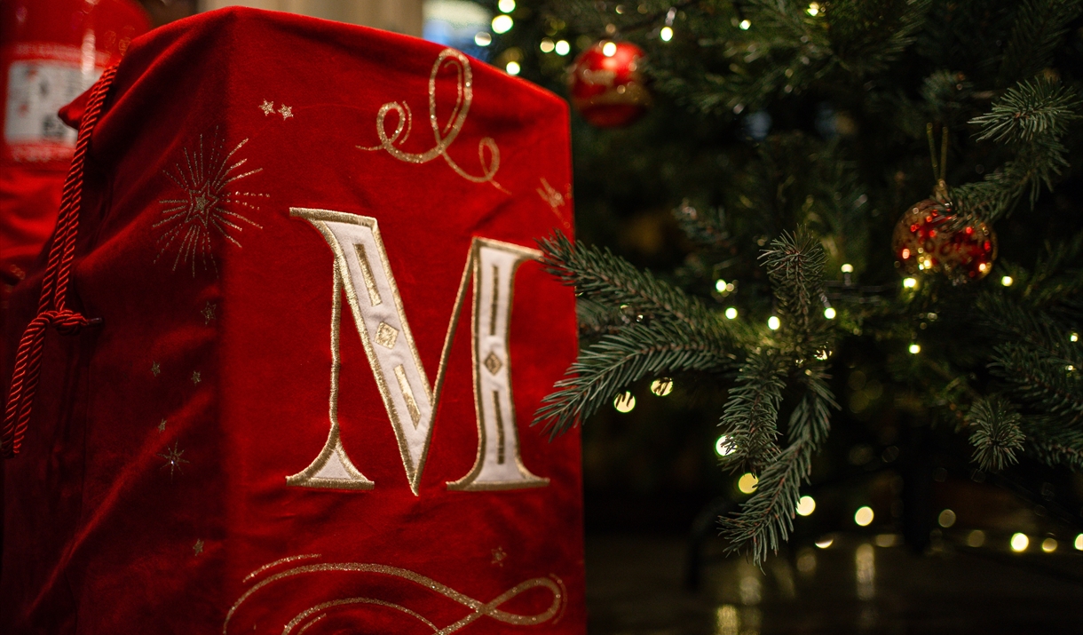 a Santa sack with the letter M on it sitting next to a Christmas tree