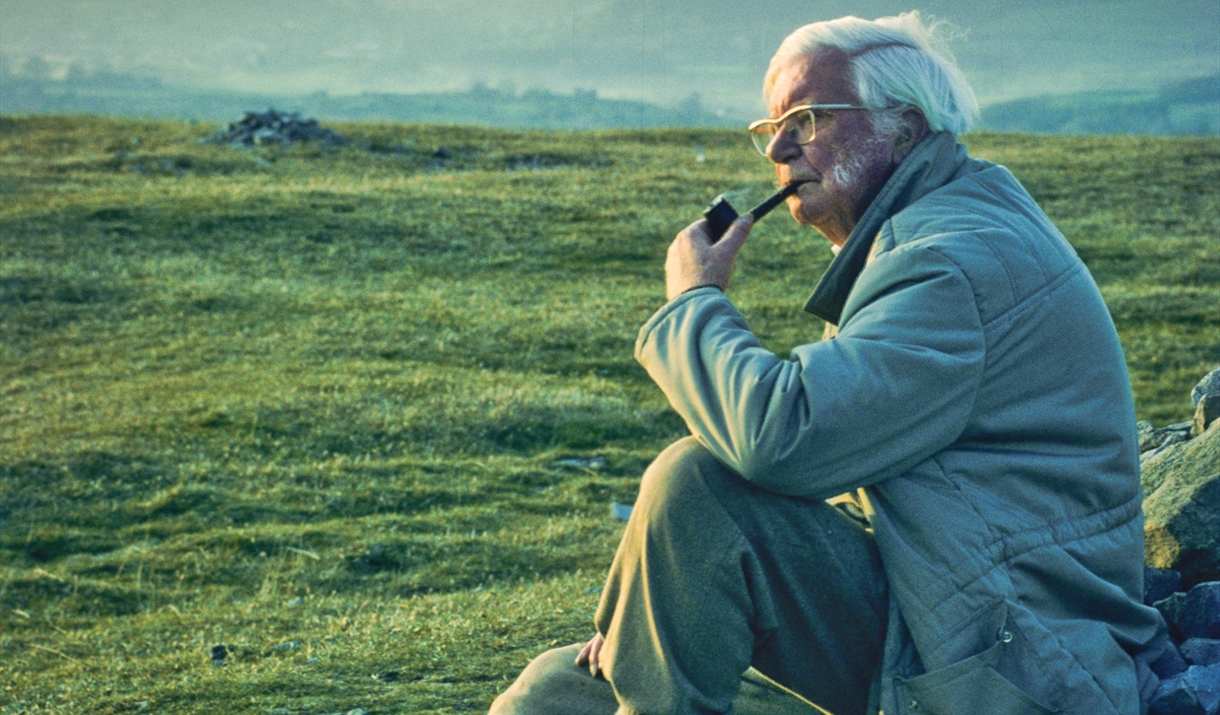 Photo of Alfred Wainwright sat smoking his pipe looking over the lake district